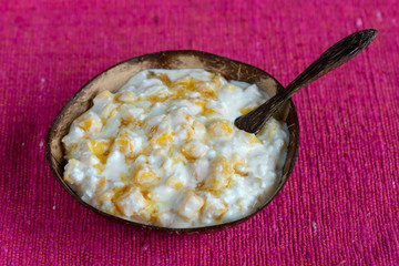 Slices of ripe sweet yellow mango fruit with white cottage cheese, honey and sour cream in coconut bowl , closeup