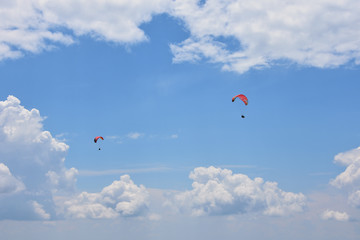 Two ram-air red tandem paragliders flying high in the blue sky with white cirrous clouds