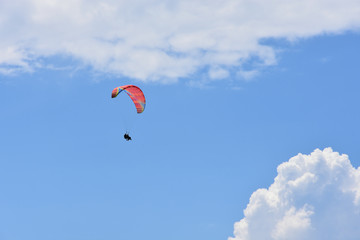 Red ram-air tandem paraglider flying high in blue sky with white cirrous clouds