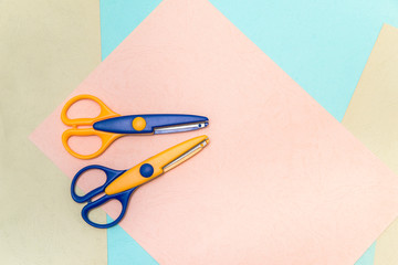 Office scissors blue and yellow for school and manual needlework, lie on colored sheets of paper. The concept of creativity, leisure and children's education.