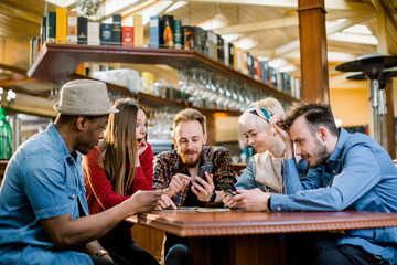 Young college students or coworkers using smartphones together at coffee shop, diverse group. Casual business, freelance work at cafe, social meeting, or education concept
