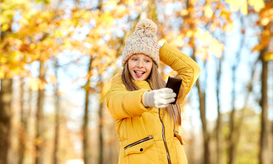 childhood, season and people concept - girl taking selfie by smartphone at autumn park