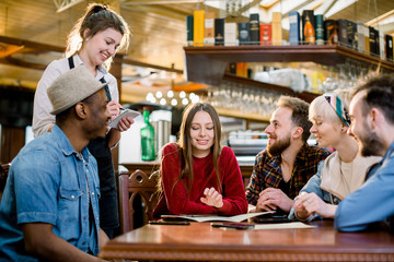 Smiling young waitress in black apron taking an order from clients in cafe. leisure, people, food cafe and holidays concept