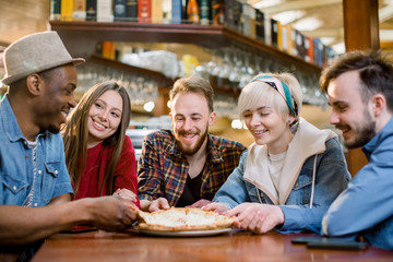Close up happy diverse friends eating pizza in cafe together, biting slices, multiracial people enjoying Italian junk food at meeting in cafeteria, having fun together, satisfied customers