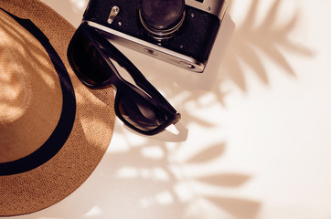 Sunglasses, hat, camera on a light background under the shadow of palm leaves.