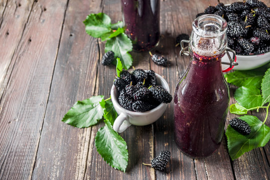 Mulberry Shrub, Juice or  liqueur in glass bottles, with fresh mulberries, rustic wooden background copy space