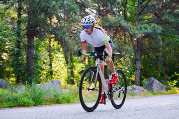 Fototapeta premium Young Woman Cyclist Riding Road Bicycle on the Free Road in the Forest at Hot Summer Day. Healthy Lifestyle Concept.