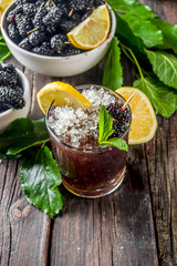 Homemade iced mulberry lemonade or mojito cocktail, with fresh mulberries, lemon slices and mint, rustic wooden background copy space