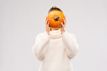 autumn, season and halloween concept - woman holding pumpkin and covering her face over grey...
