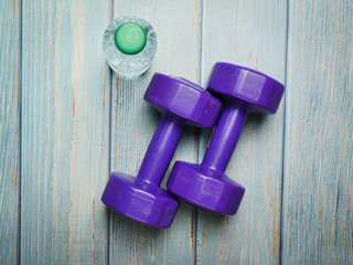 Purple dumbbells and a bottle of water on blue wooden background.