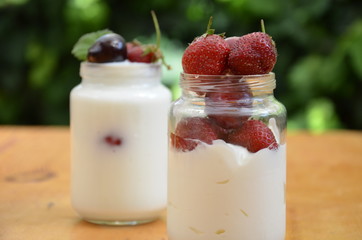 Healthy breakfast - granola, strawberries, cherry, honeysuckle berry, nuts and yogurt in a bowl. Vegetarian concept food. Top view. pudding or cocktail on the background of green foliage