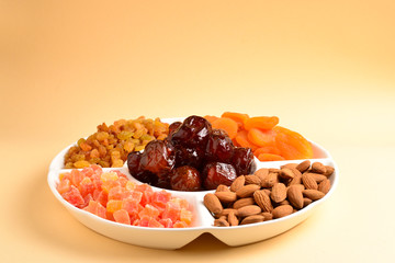Mix of dried fruits and nuts on a white plate. Apricot, almond, raisin, dates fruit. On a beige background. Space for text or design.