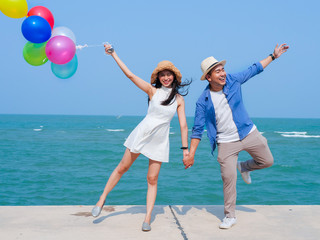 Asian couple holding colorful balloons on the beach in sunny day.