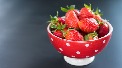 Delicious strawberries in a bowl on black background.