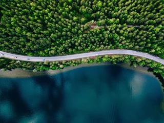 Luftaufnahme der Straße zwischen grünem Wald und blauem See in Finnland © NBLX