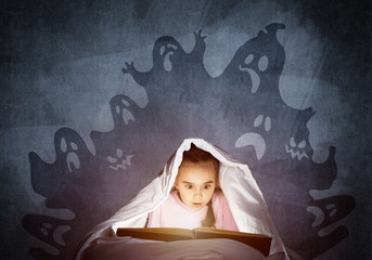 Scared little girl reading book in bed