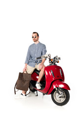 Fototapeta na wymiar full length view of handsome stylish young man sitting on red scooter and holding backpack isolated on white