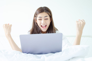 Beautiful Asian woman is smiling.Lady work with laptops on the sofa in the room in the morning.She is happy to get a new job, success, or get good news.In the white room there is a woman inside.