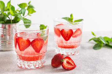 Fresh lemonade with ice, mint and strawberry in glass on white table background. Cold refreshing summer drink. Sparkling glasses with berry cocktail.