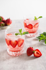 Fresh lemonade with ice, mint and strawberry in glasses on white table background. Cold refreshing summer drink. Sparkling glasses with berry cocktail.