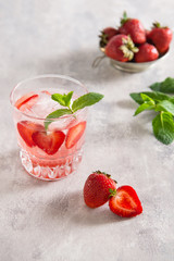 Iced tea in glass with strawberries and mint on a grey background.