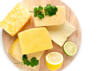 Variety of cheeses stacked on a cutting Board, on a white background with lemon and lime.