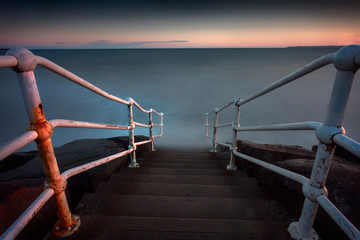 Obraz na płótnie Canvas High tide, a long exposure and a rusty handrail leading to the beach at Aberavon, Port Talbot, UK.