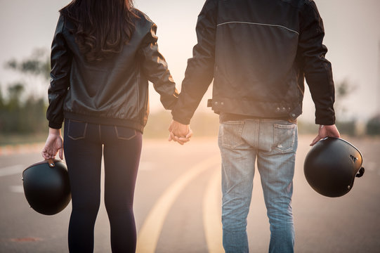 Shot of biker man and girl holding hands on the road and looks into the distance