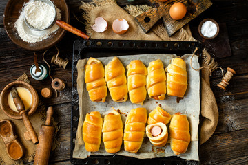 Overhead shot of delicious homemade baked sausages rolled in dough on baking tray on wooden rustic table