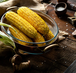 Hot boiled sweet corn in glass oval dish in copper stand with salt
