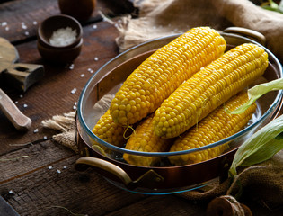 Hot boiled sweet corn in glass oval dish in copper stand with salt