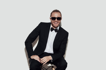 Male beauty. Charming young man in full suit looking at camera and smiling while sitting against grey background