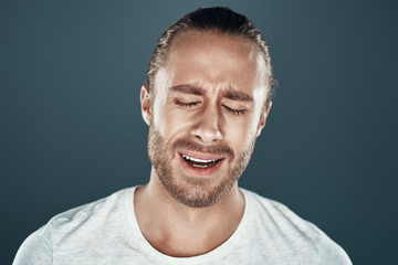 Fototapeta premium Hysteria. Frustrated young man making a face while standing against grey background
