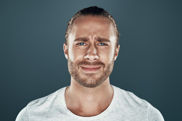 Fototapeta premium Feeling displeased. Handsome young man looking at camera while standing against grey background