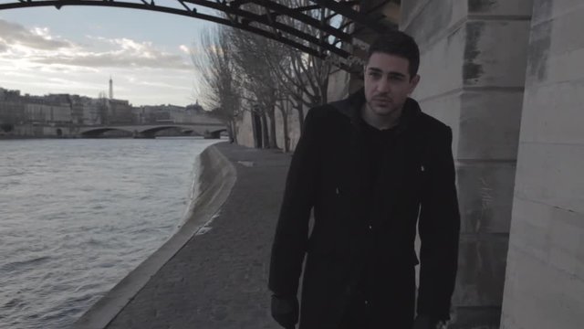 Handsome young depressed man walking on the banks of the Seine in Paris winter in the middle of the afternoon, thinking sadly to his ex girlfriend. Medium Shot.