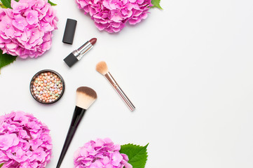 Obraz na płótnie Canvas Set of decorative cosmetics makeup brushes, blush face balls, pink hydrangea flowers on light background top view Flat lay copy space. Beauty blogger concept. Fashion background