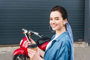beautiful girl standing near red scooter, holding paper cup with coffee and smartphone