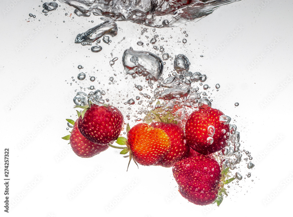 Wall mural close-up photo, on a very short exposure, strawberries falling into the water on a white background 