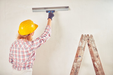 Working woman plastering / painting walls inside the house.