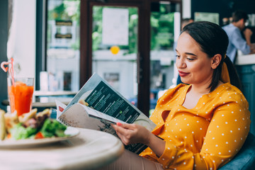 Happy beautiful plus size woman eating salad and drinking healthy smoothie in cafe