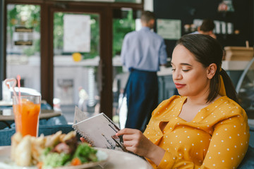 Happy beautiful plus size woman eating salad and drinking healthy smoothie in cafe