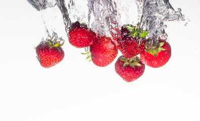 Close-up photo, on a very short exposure, strawberries falling into the water on a white background close up