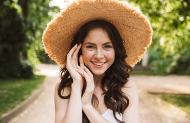 Photo closeup of seductive caucasian woman wearing straw hat smiling while walking in green park