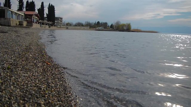 Waves are washing gravel shore. Clear lake water with small waves washing the lake shore.