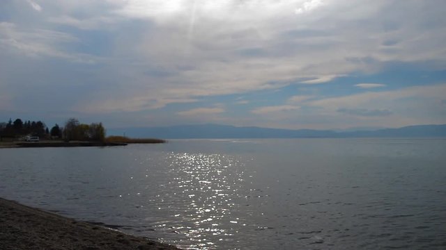 Waves are washing gravel shore. Clear lake water with small waves washing the lake shore. Panorama Landscape of a natural lake.