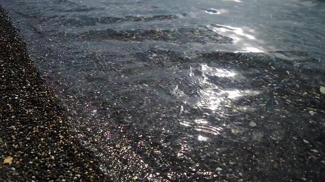 Waves are washing gravel shore. Clear lake water with small waves washing the lake shore.