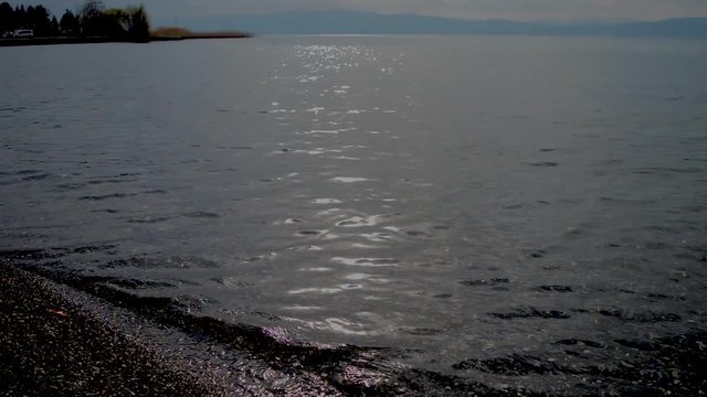 Waves are washing gravel shore. Clear lake water with small waves washing the lake shore.