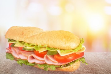 Long baguette sandwich with lettuce, vegetables, ham, and cheese on white background