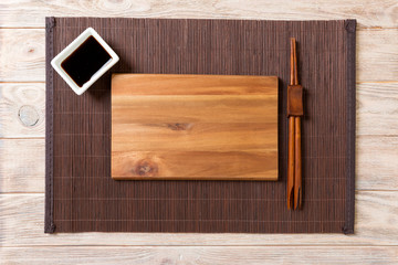 Empty rectangular wooden plate with chopsticks for sushi and soy sauce on wood background. Top view with copy space