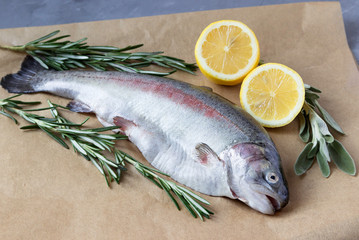 Two raw fish. Fresh trout with lemons, tomatoes and greens on the table.